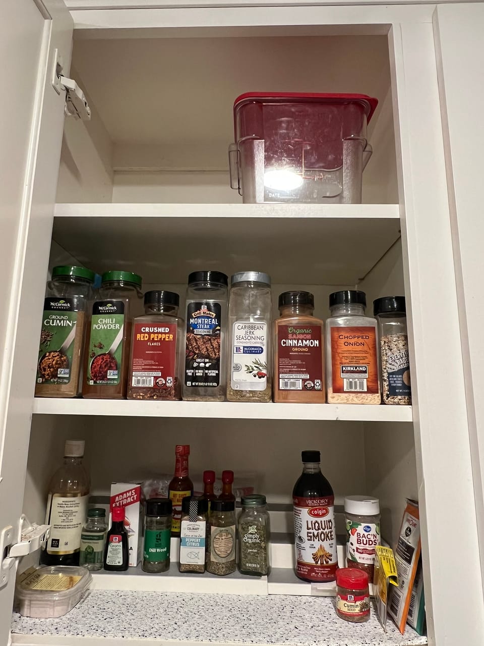 Organized spice cabinet showing neatly arranged spices and seasonings on white shelves.